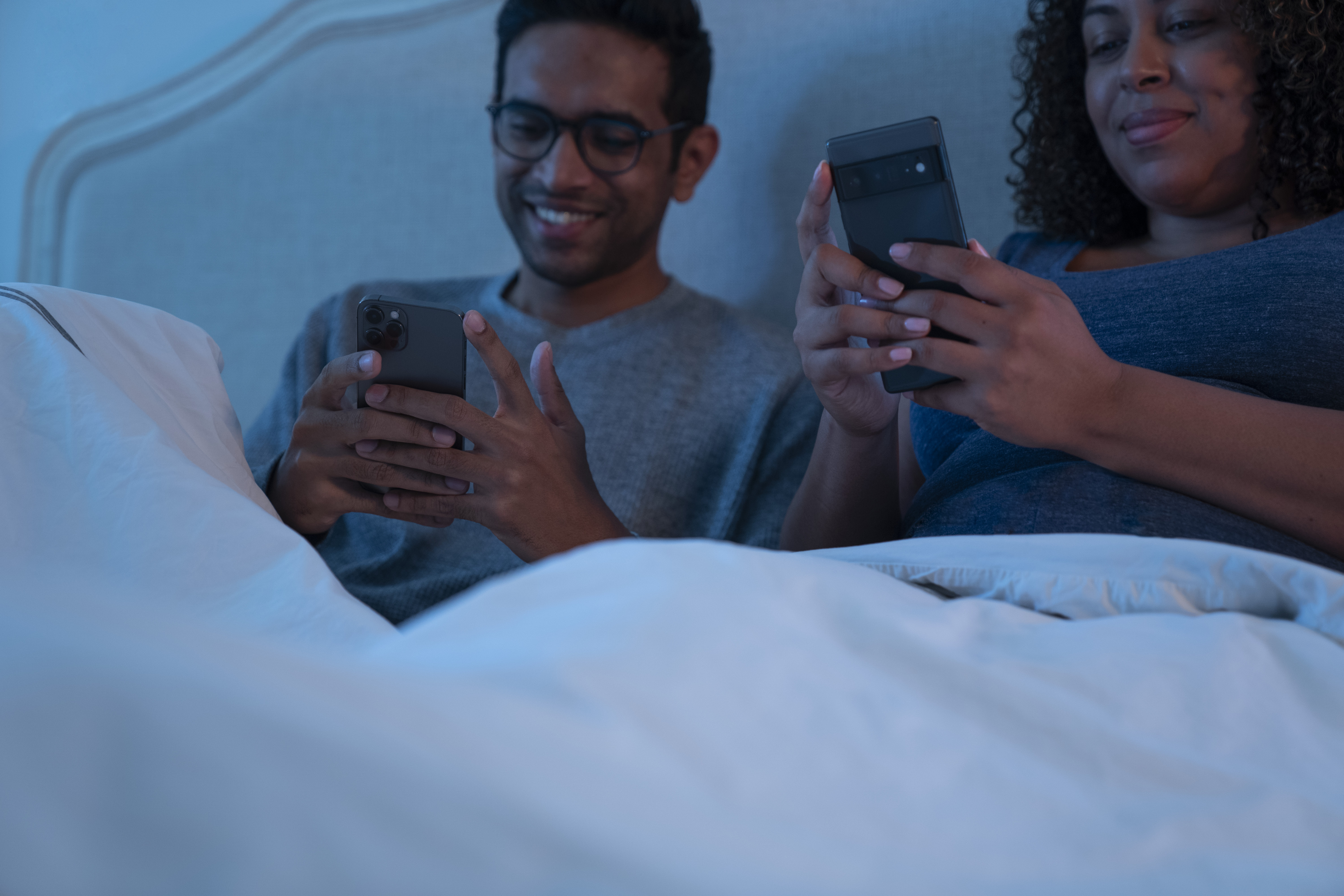 Una pareja juega con el móvil en el dormitorio.