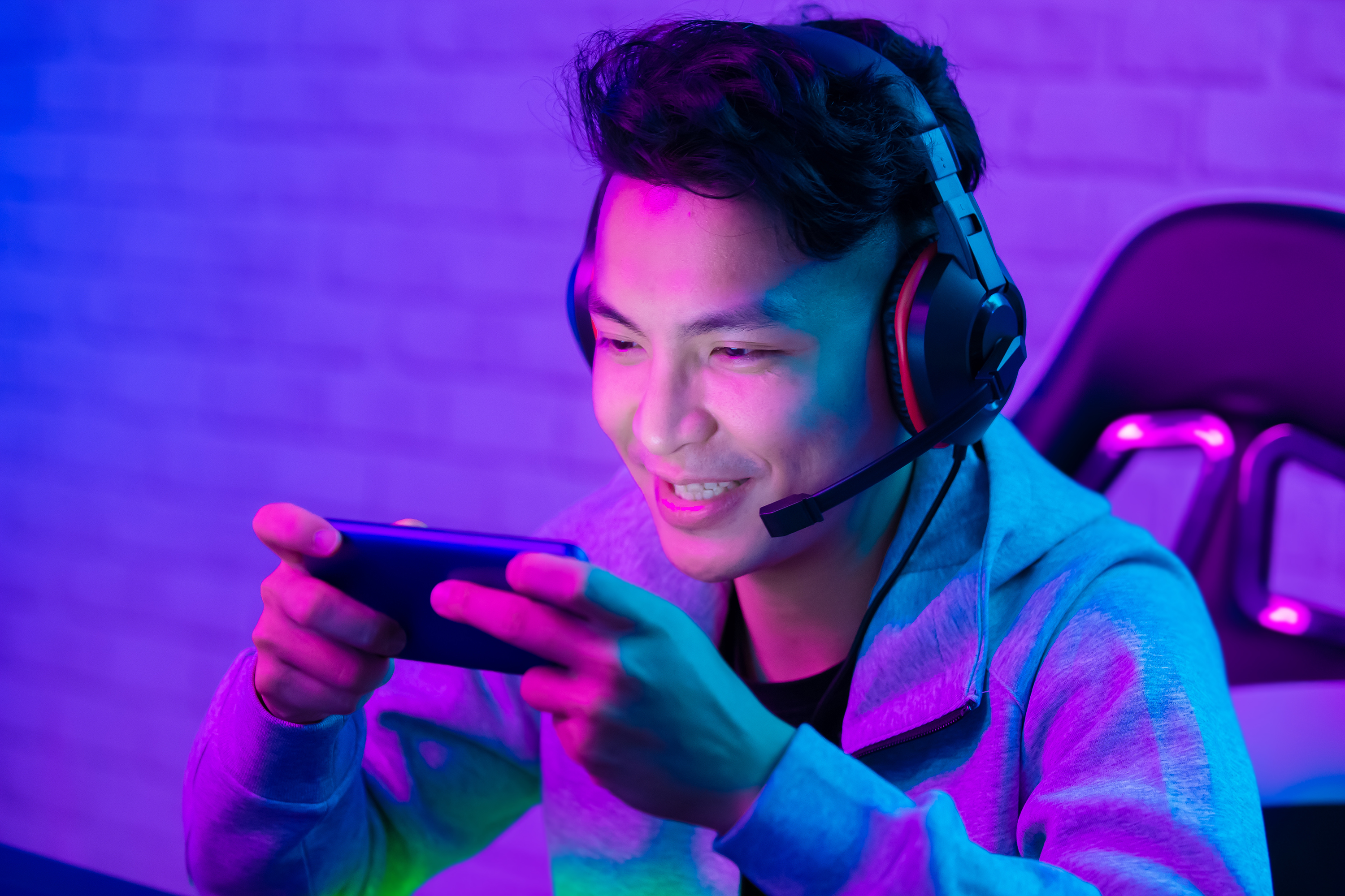 A young man wearing a gaming headset games on his cellphone.