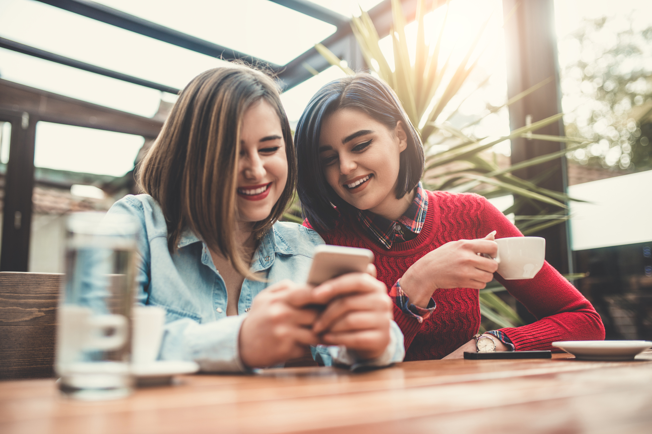 Two young women play on their phones together.