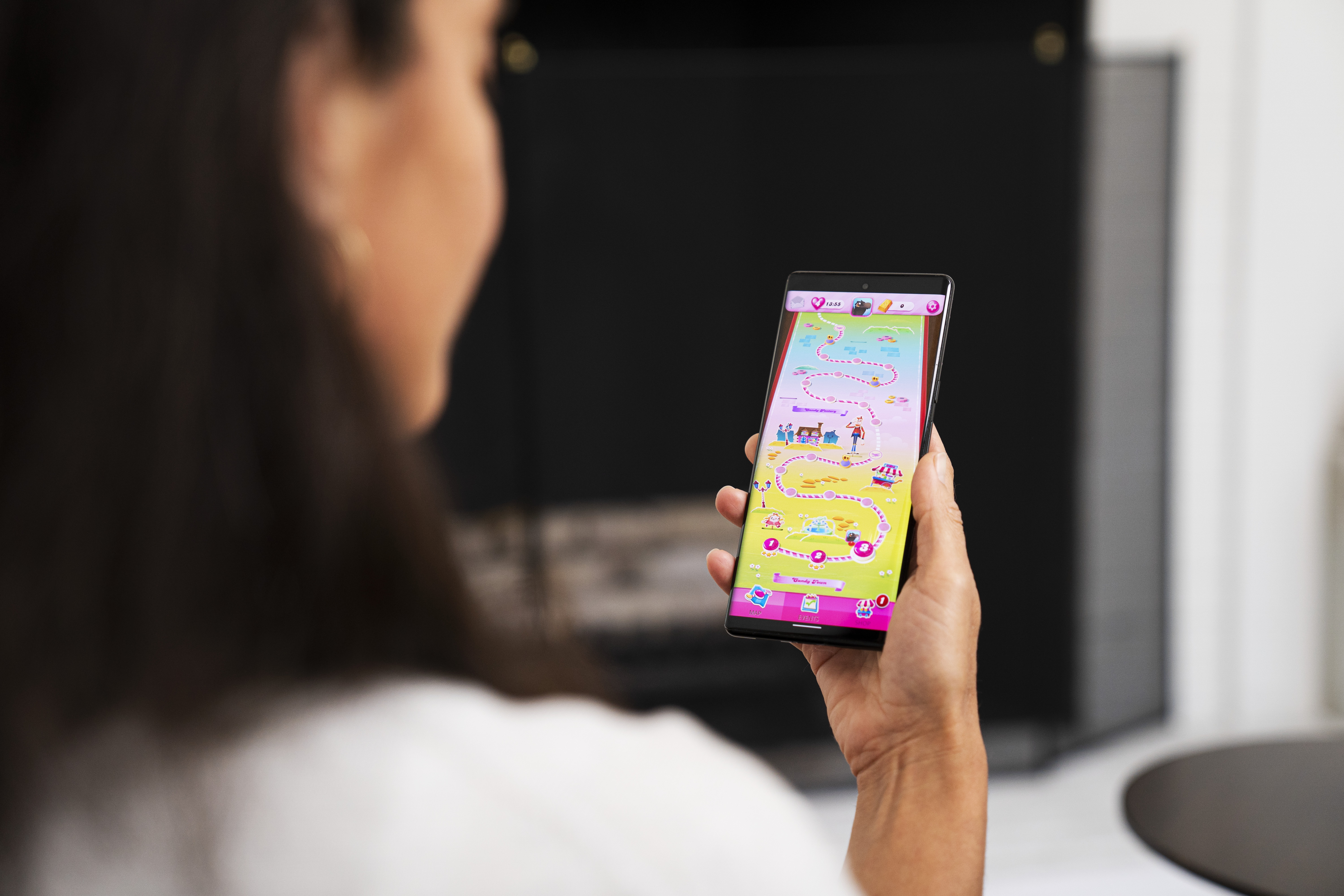 An over-the-shoulder view of a woman playing Candy Crush Saga in her living room.